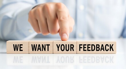Person's hand pointing at "we want your feedback" wooden blocks
