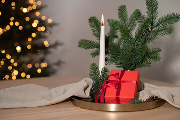 Festive Christmas holiday background, candle light, red gift box, fir tree branches on table with blurred shiny golden lights background, neutral winter lifestyle home interior