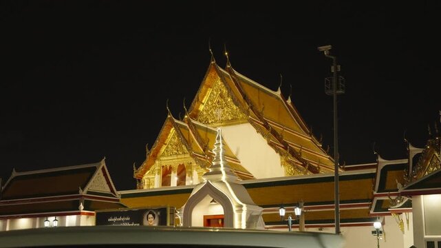Night view of a traditional Thai temple roof glowing with golden lights against the dark Bangkok sky.