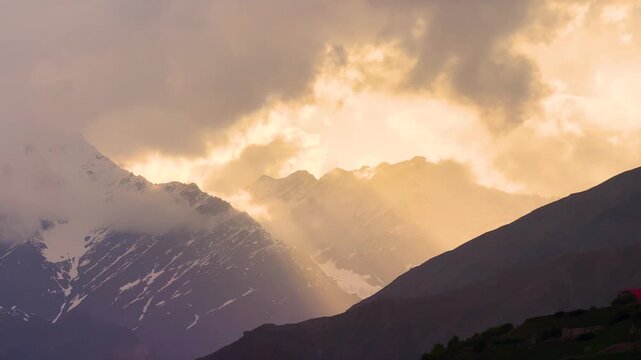 4K shot of orange sky above the Himalayan mountain peaks surrounded by clouds during the winter season as seen from Khangsar village in Lahaul Valley, Himachal Pradesh, India. Scenic sunset background