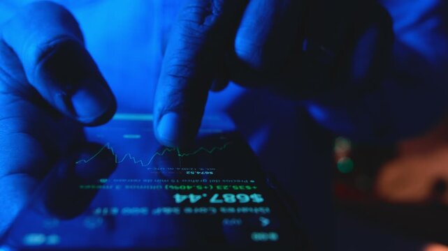 Close-up of hands holding a smartphone, analyzing financial data and stock market graphs at night