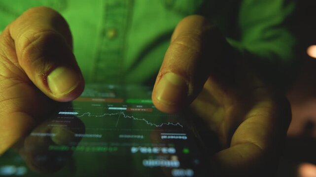 Close-up of a trader's finger scrolling through a financial graph on a digital device at night