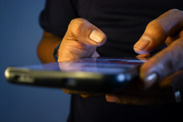 Closeup top view of Asian man using smartphone in dark room, browsing internet and scrolling screen with finger. Close-up of man hand scrolling using mobile phone social media in dimly lit setting.
