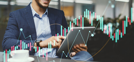 A milennial businessman of Middle Eastern descent sits at a table in a modern office, happily using a tablet to check out the latest business mobile application, surrounded by greenery.