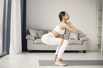 Brunette fit woman in white leggins and top working out on mat at home