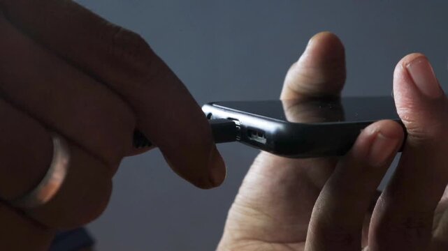 Close-up of an Asian man's hand plugging a charging cable into a phone. Concept of contemporary technology convenience.