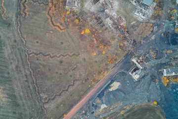 Aerial top down view of zigzag military trenches near coal mine slag and destroyed buildings. War zone frontline contrast and industrial pollution.