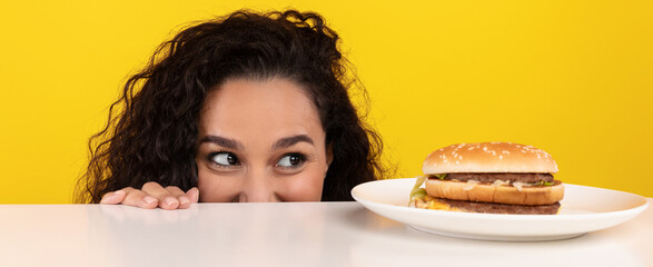 A woman with curly hair is peeking over a table, her eyes wide with excitement as she gazes at a...