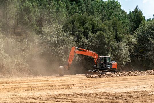 Escavadora a trabalhar em terraplanagem numa obra de autoestrada, levantando uma densa nuvem de poeira numa zona arborizada