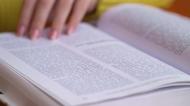 Close-up of hands turning pages and reading open book with detailed text