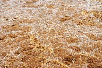 Smudged water flows profusely. River water flowing profusely. Flood waters rushing down river after storm flows through. Turbulent river dam. Water turbulence of river due to dam. Water Nature Texture