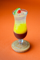 Cóctel tropical de capas con hielo sobre fondo naranja