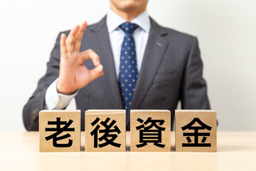 「老後資金」と書かれたブロックとOKポーズをするビジネスマン