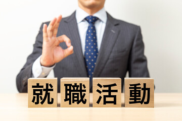 「就職活動」と書かれたブロックとOKポーズをするビジネスマン