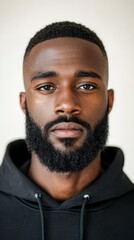 Obraz premium Young man exhibits a confident demeanor with a short haircut and beard while wearing a black hoodie in a neutral space Generative AI