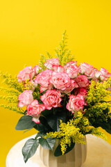 Arreglo floral de rosas rosadas sobre fondo amarillo minimalista
