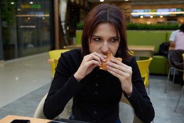  A girl is eating a sandwich while sitting at a table in a cafe