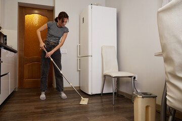 Woman mops floor in modern kitchen during afternoon