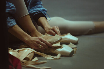 Closeup of hands preparing ballet shoes on studio floor. Concept of equipment readiness, backstage workflow, dance preparation guides and educational materials.