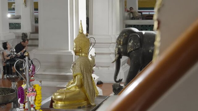 A serene golden Buddha figure displayed on a decorated altar with offerings nearby.
