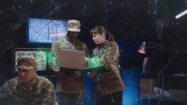 Group of military personnel standing in dark command room. Working together while checking laptop and documents. Holograms floating in air showing tactical data. Multiple screens glowing.