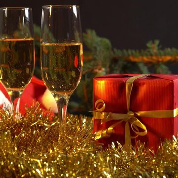 Bicchieri di vino in primo piano decorazioni natalizie con pacchetti, luci colorate intermittenti, video 1:1