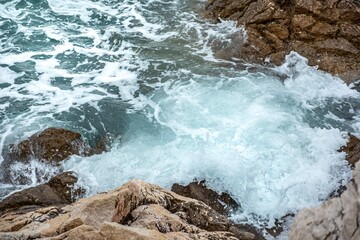Sea waves and ocean water foam splash against rocks on the coastline. Powerful nature scene for travel, wellness and marketing designs.