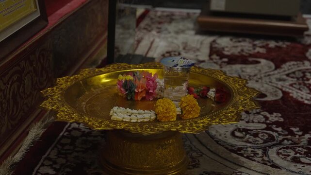 A traditional golden pedestal tray holding fresh jasmine flower garlands meant for religious offerings.