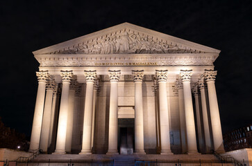 Illuminated La Madeleine church stands with Corinthian columns in Paris, France. Neoclassical Catholic temple features majestic stone facade and pediment sculpture under night sky