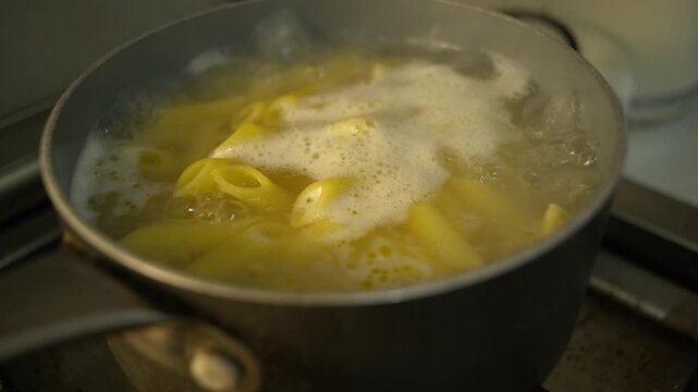 Close-up isolated gritty every day style grunge dark documentary shot of gluten free penne pasta boiling in a saucepan with water bubbling on the surface