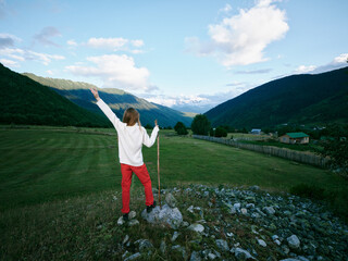 Fototapeta premium Hiker outdoors mountains valley scenery with freedom and exploration as arms rise on a rocky hillside, walking stick raised toward the expansive horizon beneath blue skies.