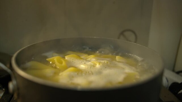 Close-up isolated gritty every day style grunge dark documentary shot of gluten-free penne pasta boiling in a saucepan with water bubbling on the surface with a warning sign sticker in the background