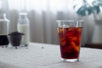 Cold brew coffee in a clear glass with ice on a table covered with a natural linen tablecloth.