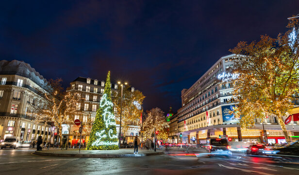 Paris, France - December 8, 2025: Illuminated Christmas tree stands at Place Diaghilev near Galeries Lafayette on Boulevard Haussmann. Festive holiday installation features neon lights under night sky