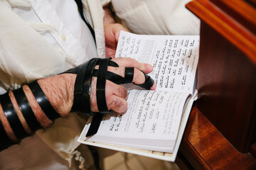 Close-up of Jewish Man's Hand Wearing Tefillin and Reading from a Holy Book or Prayer Book (Siddur) During Religious Study or Bar Mitzvah