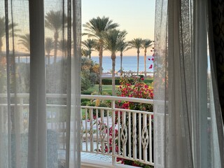 Fototapeta premium View from the room onto the balcony and the turquoise sea with the resort's palm trees at sunset. Travel destinations. Summer vacations. Year-round vacations