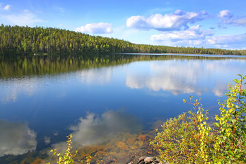 Beautiful landscape with a calm clear lake which has reflections of the trees and clouds. The lake lies within the Arctic circle near Polcirkeln, Northern Sweden, Scandinavia. © lisastrachan