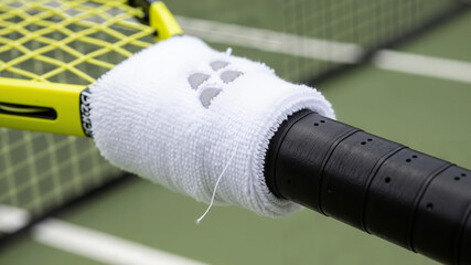Tennis racket handle wrapped with white sweatband on court  