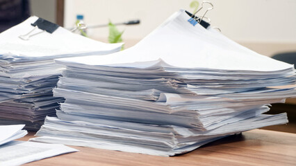 Huge stacks of sorted paper documents with black binder clips on a wooden office desk. Concept of bureaucracy and heavy administrative workload. Photo