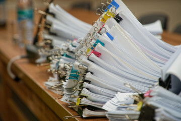 Huge stacks of sorted paper documents with colorful binder clips on a wooden office desk. Concept of bureaucracy and heavy administrative workload. Photo