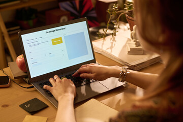 Caucasian young adult woman typing on laptop using AI image generator software at wooden desk, hands on keyboard, digital workspace with office supplies and documents visible