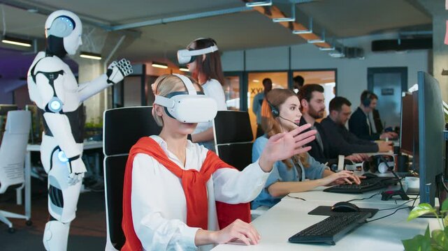 Female rotating virtual object with hands in VR headset. Coworkers typing at computers nearby. Woman in background using controllers in simulation. Humanoid robot observing activity.