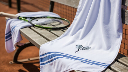 Tennis towels and racket resting on wooden bench at outdoor court
