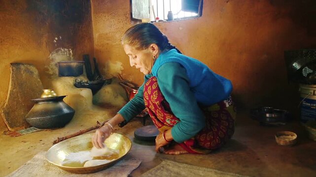 An elderly Indian woman aged over seventy prepares food on a traditional stove inside a rural home. The scene reflects village lifestyle, traditional cooking, resilience, and everyday life in India.
