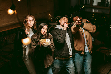 Friends celebrate a birthday at a cozy cafe during the evening with cake and cheerful laughter