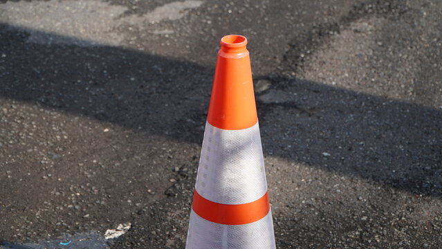 A high-angle shot of an orange and white traffic cone standing on dark, sunlit asphalt ground.