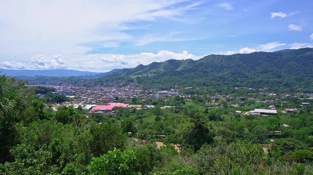 Aerial panning shot of Tingo Maria town beside the Huallaga River surrounded by lush Amazon rainforest mountains and vibrant tropical landscape in Peru.