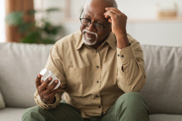 An older man sits on a couch, displaying concern as he examines a bottle of medication. The setting is cozy, illuminated by soft evening light, hinting at his contemplation.