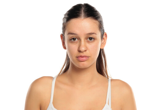 Studio shot of a natural woman with long dark hair wearing a white top, without makeup, neutral expression, portrait on a white background