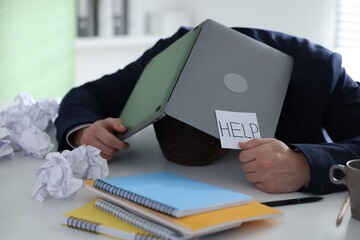 Man with laptop and sign Help at table in office
